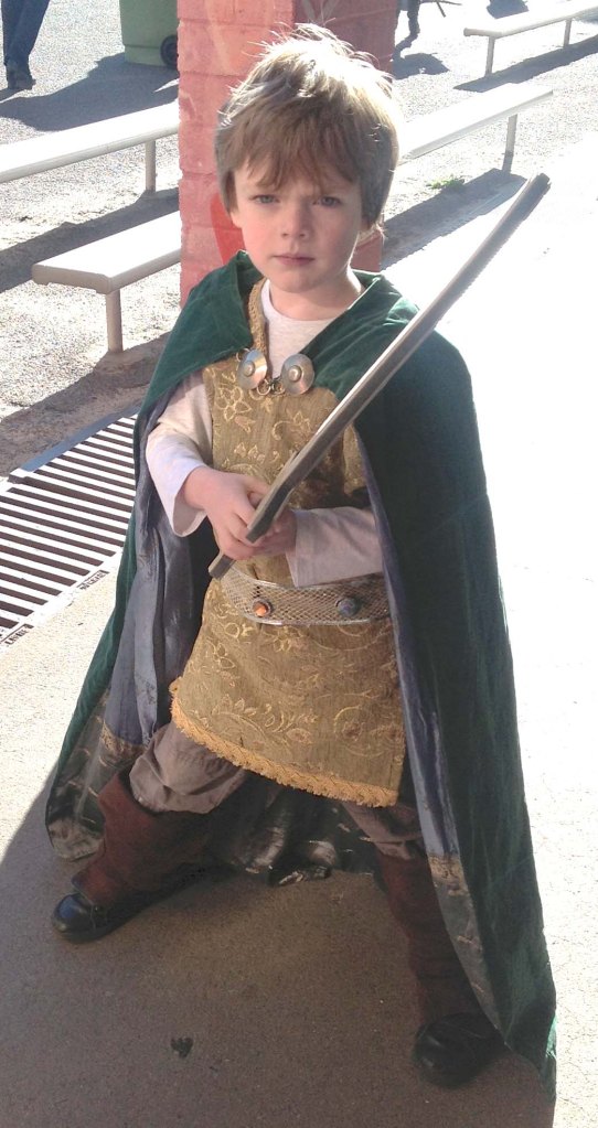 Five year old boy in cloak holding sword.